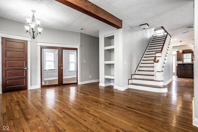 entrance foyer featuring beamed ceiling, french doors, dark wood-type flooring, a notable chandelier, and a textured ceiling