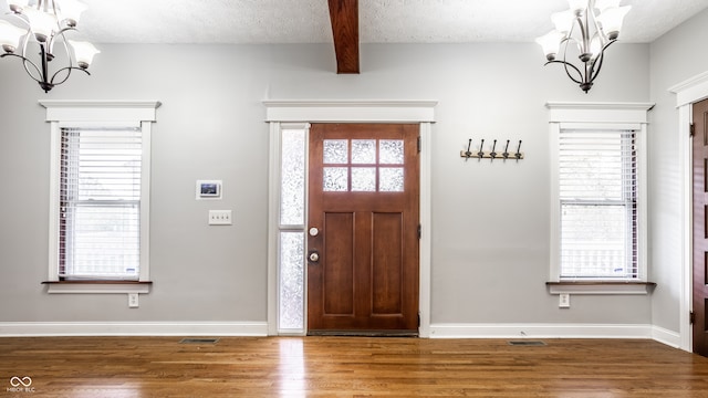 foyer featuring a notable chandelier, beam ceiling, hardwood / wood-style floors, and a textured ceiling