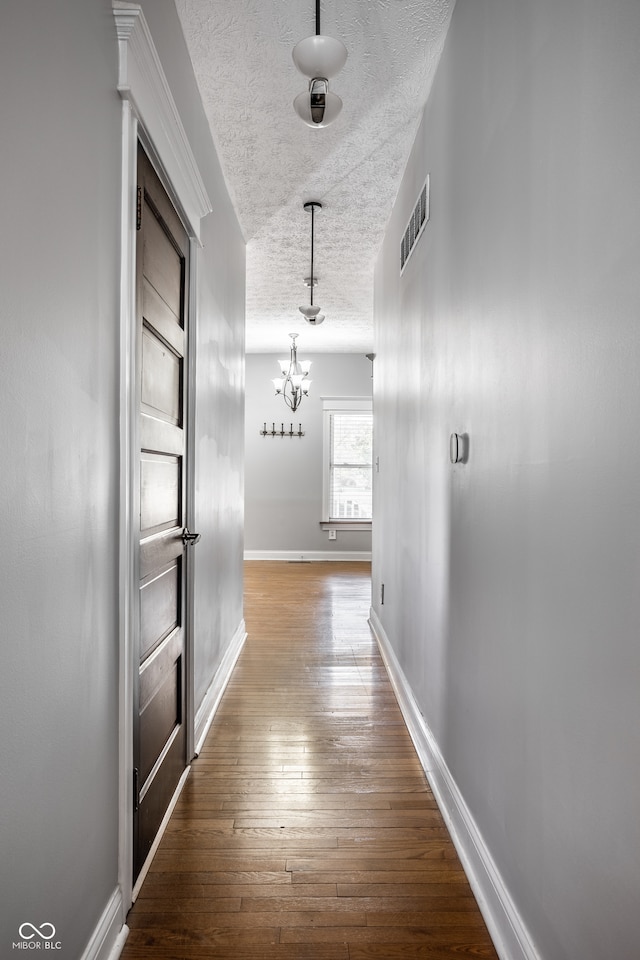 hall with wood-type flooring, a textured ceiling, and an inviting chandelier