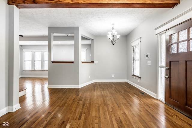 foyer entrance with a textured ceiling, a notable chandelier, and dark hardwood / wood-style flooring