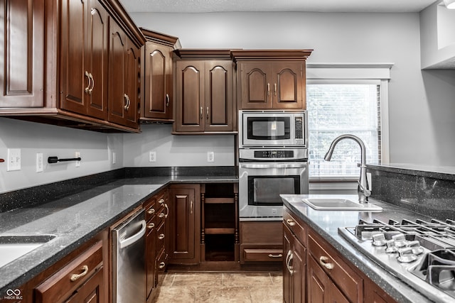 kitchen featuring appliances with stainless steel finishes, dark stone countertops, dark brown cabinetry, and sink