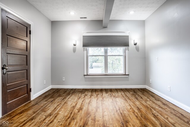 spare room with hardwood / wood-style flooring, beam ceiling, and a textured ceiling