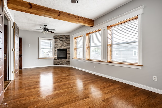 unfurnished living room with beamed ceiling, ceiling fan, a stone fireplace, dark hardwood / wood-style floors, and a textured ceiling