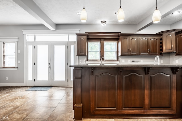 kitchen featuring dark brown cabinets, dark stone countertops, beam ceiling, and hanging light fixtures