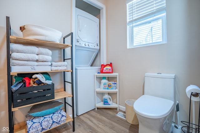 bathroom featuring stacked washer and clothes dryer, hardwood / wood-style flooring, and toilet