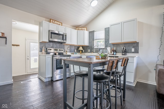 kitchen featuring white cabinets, lofted ceiling, appliances with stainless steel finishes, dark hardwood / wood-style floors, and decorative backsplash