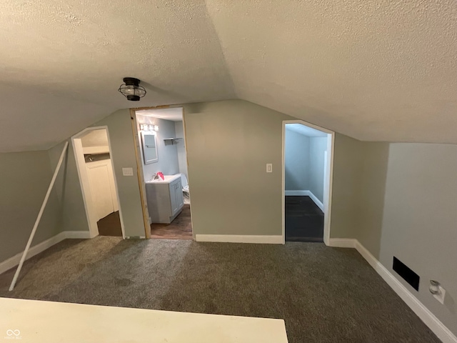 additional living space featuring dark carpet, a textured ceiling, and vaulted ceiling