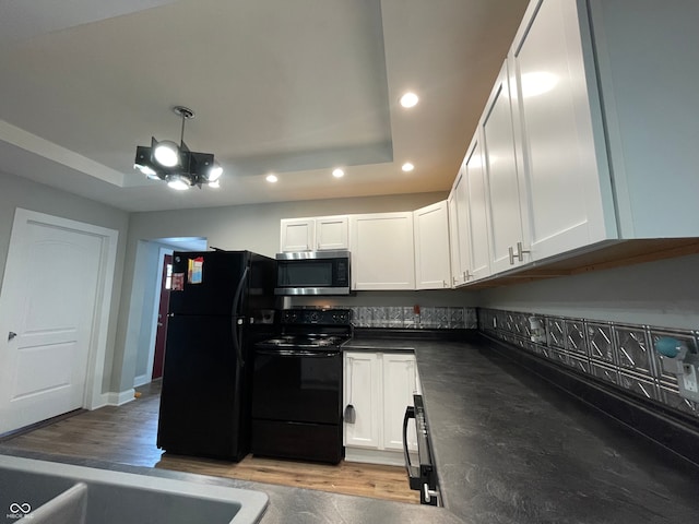 kitchen featuring light wood-type flooring, black appliances, a raised ceiling, and white cabinets