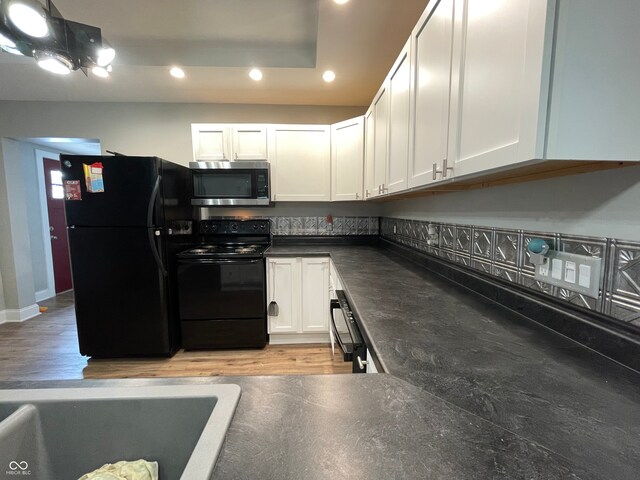 kitchen with light wood-type flooring, black appliances, and white cabinets