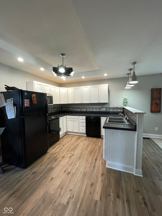 kitchen with white cabinets, hanging light fixtures, kitchen peninsula, black appliances, and light wood-type flooring