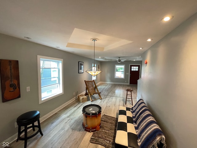 living room with ceiling fan, light wood-type flooring, and a raised ceiling