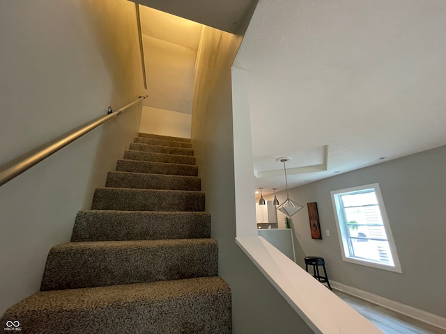 staircase featuring wood-type flooring and a raised ceiling