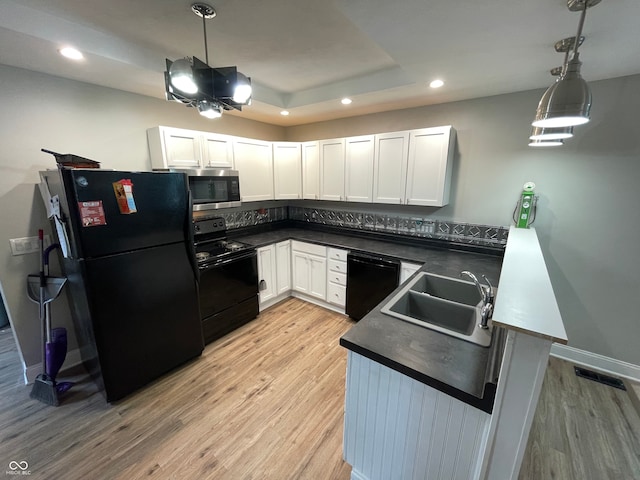 kitchen with pendant lighting, black appliances, white cabinetry, and light hardwood / wood-style flooring