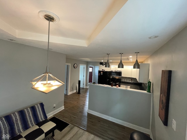 interior space with white cabinets, kitchen peninsula, decorative light fixtures, black refrigerator, and dark hardwood / wood-style flooring