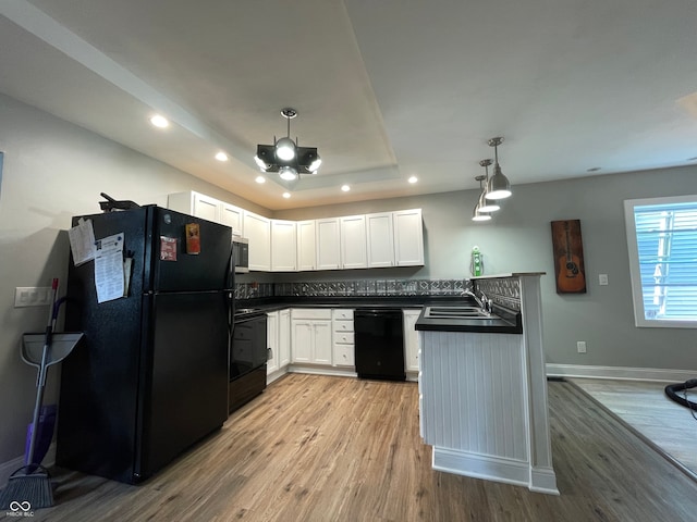 kitchen with hanging light fixtures, kitchen peninsula, white cabinetry, black appliances, and light hardwood / wood-style floors