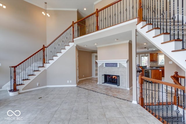 unfurnished living room featuring beverage cooler, a towering ceiling, a tile fireplace, and crown molding