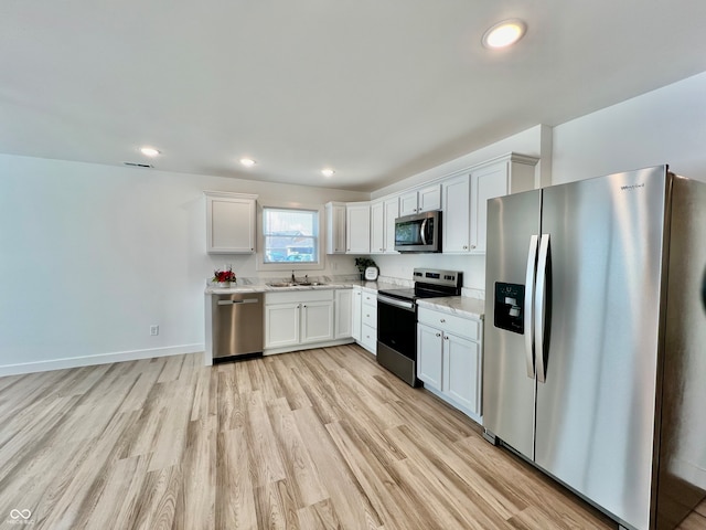 kitchen with appliances with stainless steel finishes, light wood-type flooring, white cabinetry, and sink