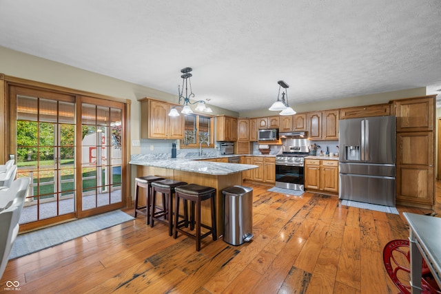 kitchen with kitchen peninsula, appliances with stainless steel finishes, a kitchen bar, light hardwood / wood-style flooring, and decorative light fixtures