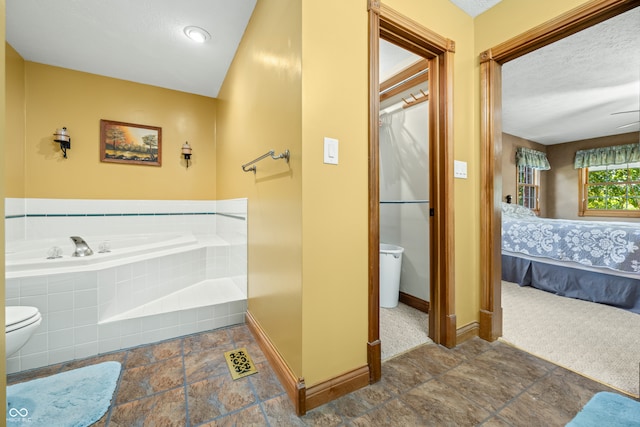 bathroom with tiled bath, a textured ceiling, and toilet