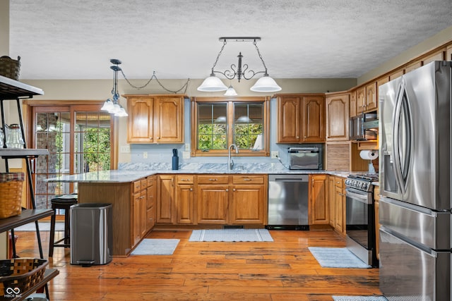 kitchen with a wealth of natural light, appliances with stainless steel finishes, hanging light fixtures, and kitchen peninsula