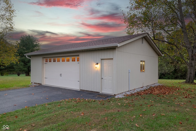 garage at dusk featuring a lawn