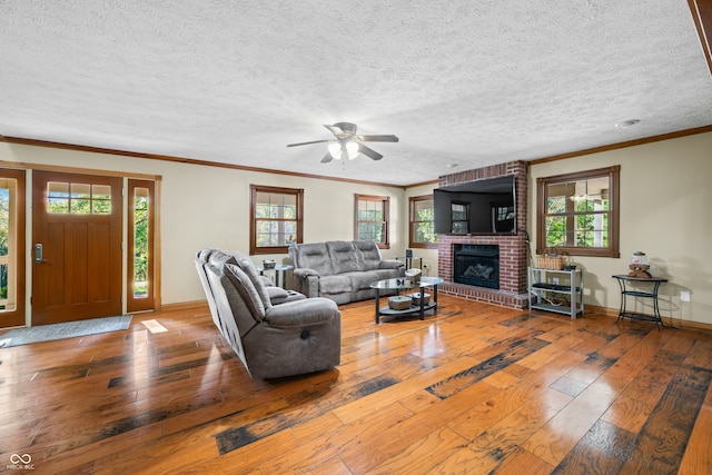 living room with ceiling fan, a textured ceiling, wood-type flooring, a brick fireplace, and ornamental molding