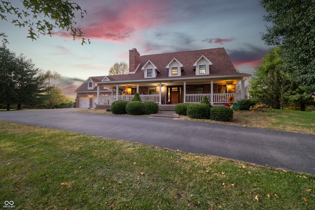 cape cod house featuring covered porch, a garage, and a lawn