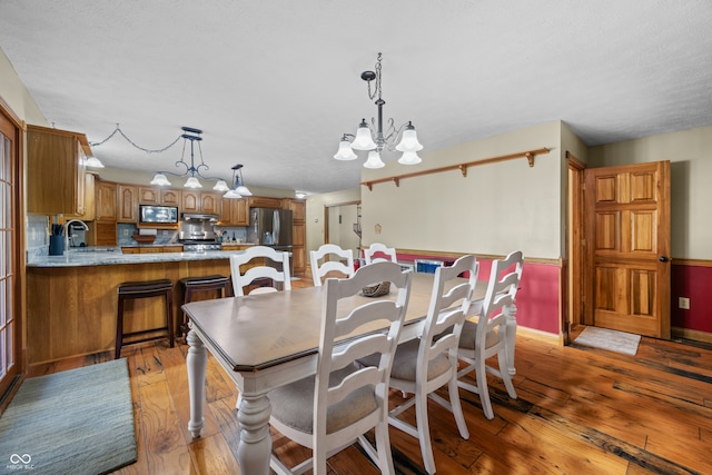 dining room with light hardwood / wood-style floors, a textured ceiling, sink, and a chandelier