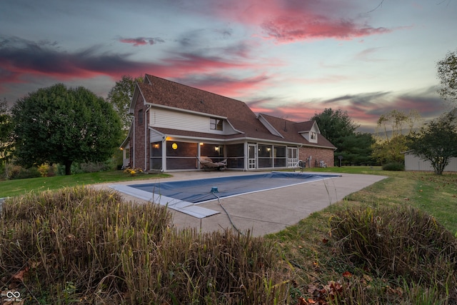 pool at dusk featuring a patio area, a lawn, and a sunroom