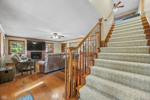 stairway featuring ceiling fan, a textured ceiling, wood-type flooring, a fireplace, and crown molding