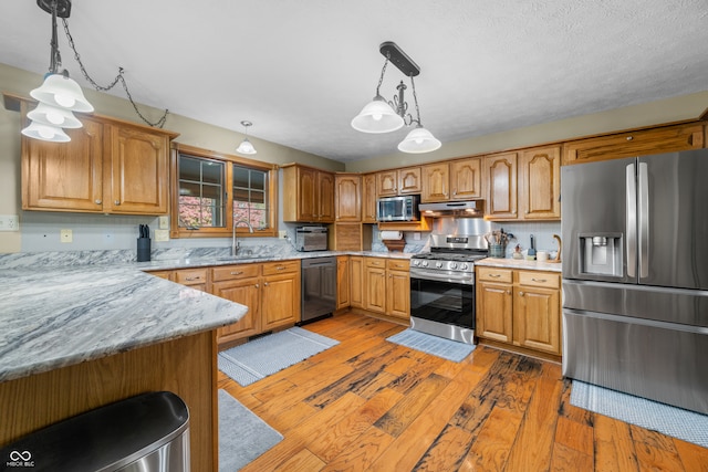 kitchen with appliances with stainless steel finishes, sink, kitchen peninsula, pendant lighting, and dark wood-type flooring