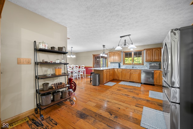 kitchen with appliances with stainless steel finishes, a textured ceiling, light hardwood / wood-style floors, pendant lighting, and a notable chandelier