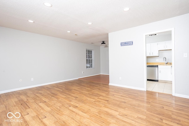 unfurnished living room with sink, light hardwood / wood-style flooring, and a textured ceiling