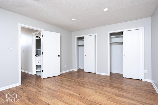 unfurnished bedroom with multiple closets, light hardwood / wood-style flooring, and a textured ceiling