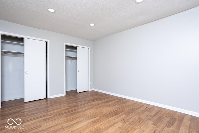 unfurnished bedroom featuring hardwood / wood-style floors, a textured ceiling, and two closets