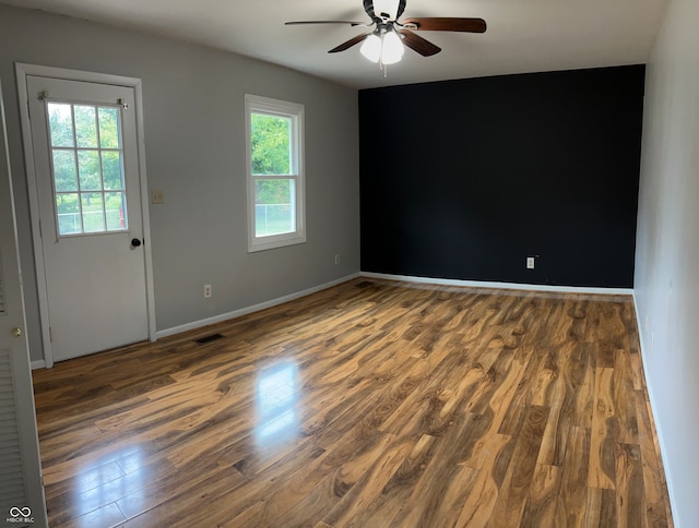 empty room with ceiling fan, plenty of natural light, and dark hardwood / wood-style floors