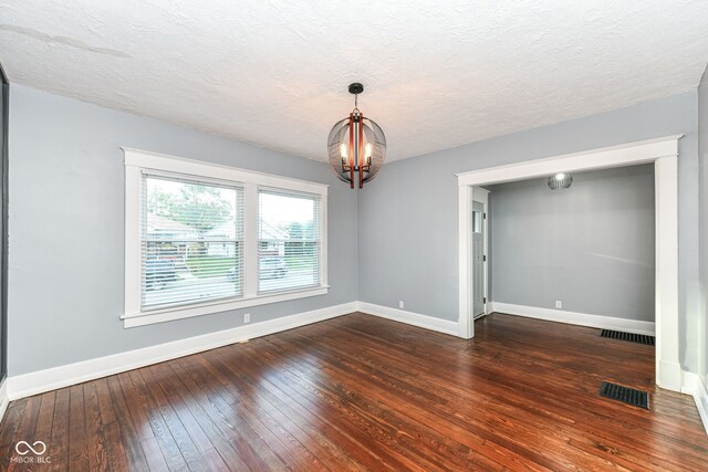 empty room with dark hardwood / wood-style floors, a textured ceiling, and a chandelier