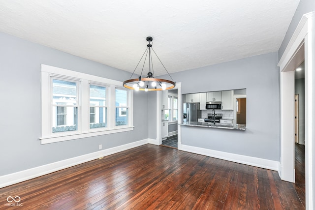 unfurnished dining area featuring a notable chandelier, dark hardwood / wood-style flooring, and a textured ceiling