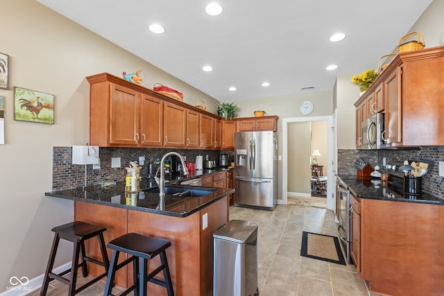 kitchen with kitchen peninsula, backsplash, appliances with stainless steel finishes, dark stone counters, and sink