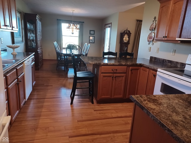 kitchen featuring a breakfast bar area, white appliances, a notable chandelier, decorative light fixtures, and light hardwood / wood-style floors