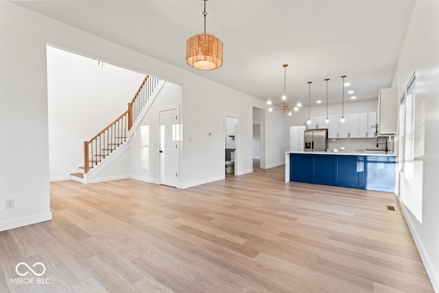 kitchen featuring stainless steel refrigerator with ice dispenser, white cabinets, hanging light fixtures, and light wood-type flooring