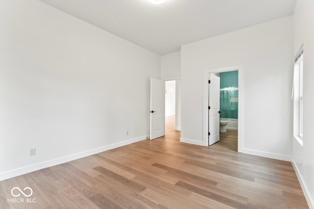 unfurnished bedroom with ensuite bath, multiple windows, and light hardwood / wood-style floors