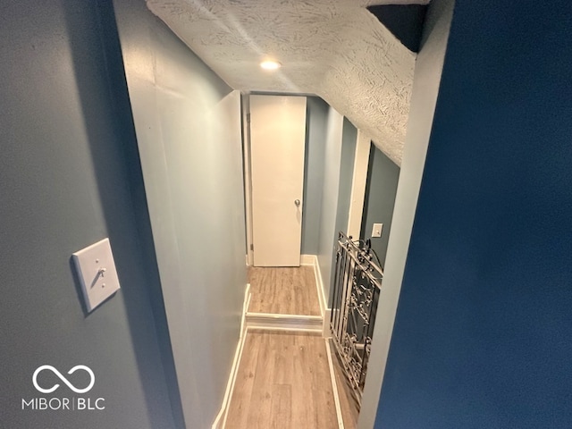 hall featuring light hardwood / wood-style floors, a textured ceiling, and lofted ceiling