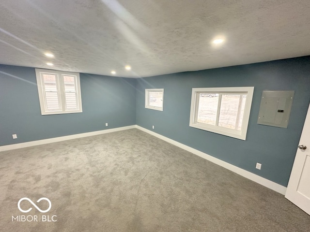 carpeted spare room featuring a textured ceiling, electric panel, and plenty of natural light