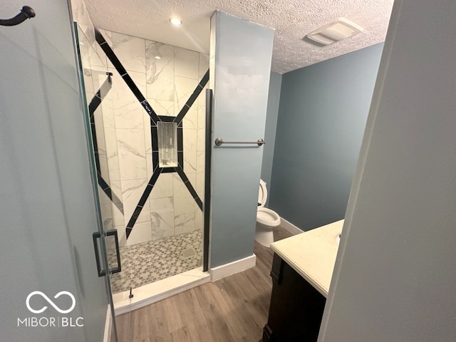 bathroom with a textured ceiling, walk in shower, wood-type flooring, toilet, and vanity