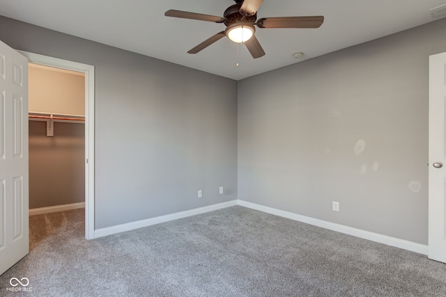 unfurnished bedroom with a closet, a spacious closet, light colored carpet, and ceiling fan