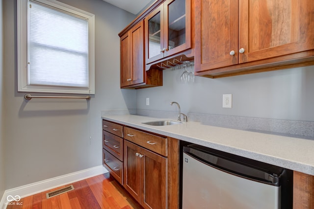 kitchen with stainless steel dishwasher, sink, and light hardwood / wood-style flooring