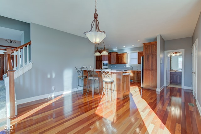 kitchen featuring a kitchen island, hanging light fixtures, stainless steel fridge, a breakfast bar, and light hardwood / wood-style floors