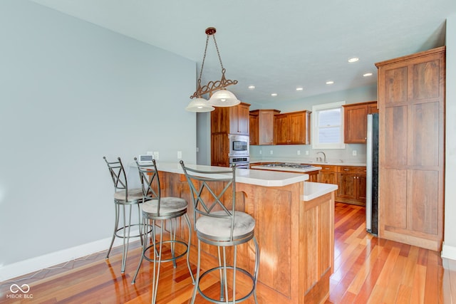 kitchen with a kitchen bar, a center island, stainless steel appliances, decorative light fixtures, and light hardwood / wood-style flooring