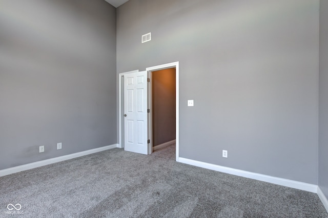 carpeted empty room featuring a towering ceiling